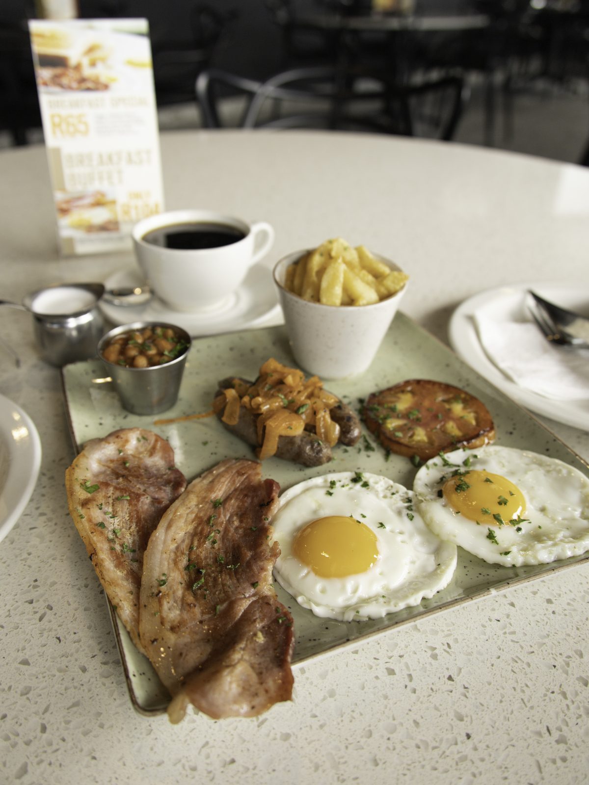 A full breakfast of bacon, eggs, sausage, beans and chips with coffee