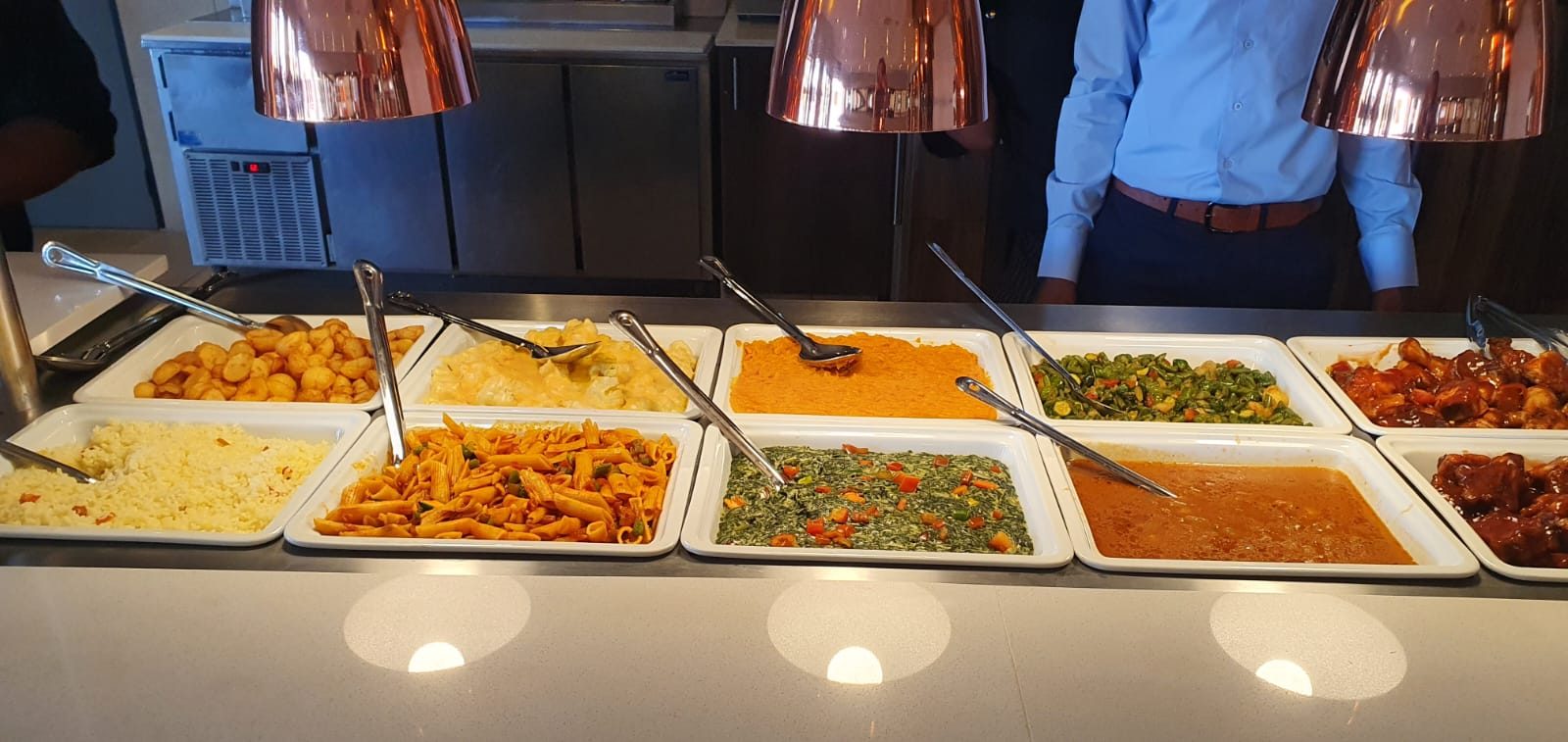 Buffet trays of rice, pasta, vegetables and stews under warming lamps